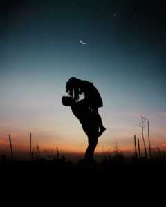 man lifting woman in silhouette at night