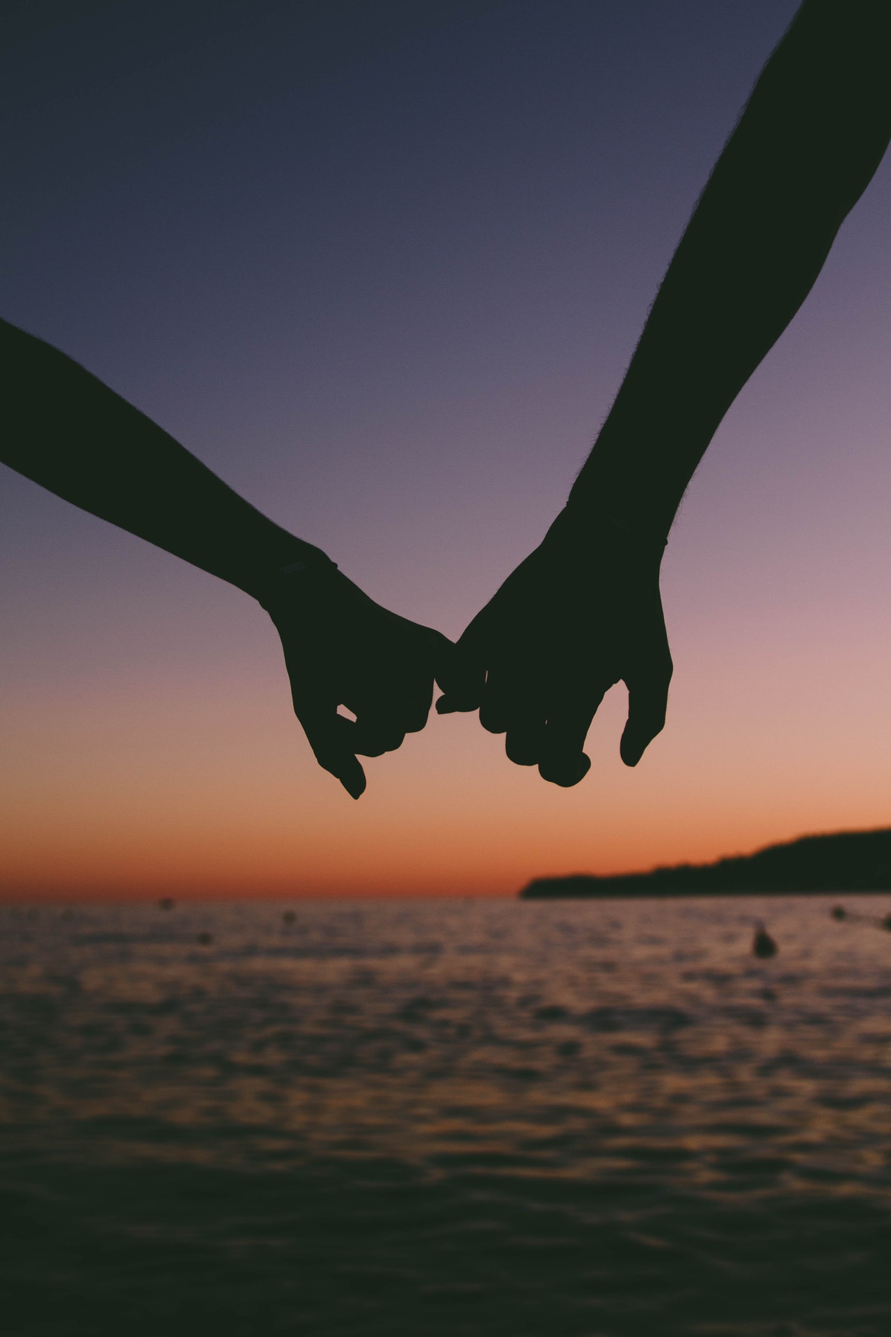 couple holding pinkies at sunset on the beach