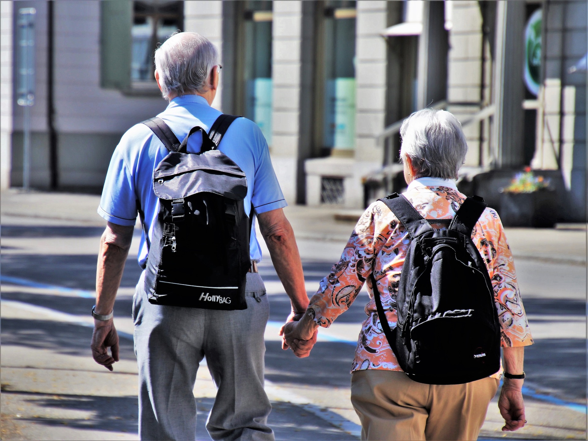 older couple holding hands with backpacks