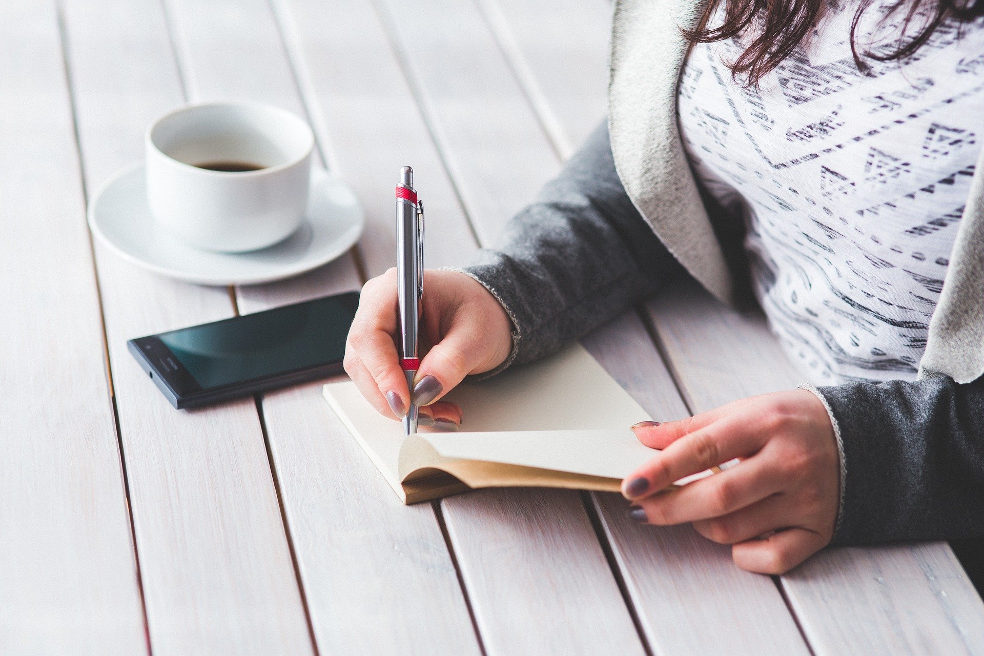 woman writing with coffee and phone